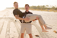 A male ambassador holding another male ambassador in his arms on the beach