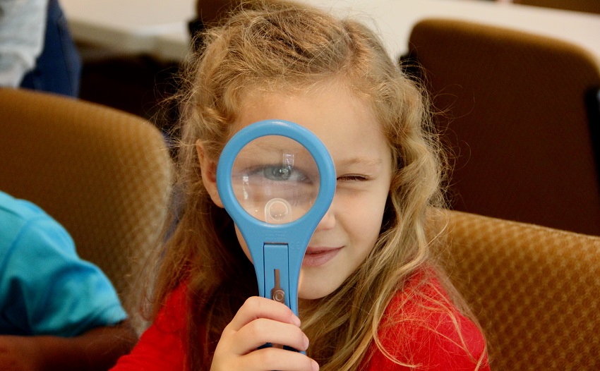 girl child looking through magnifying glass