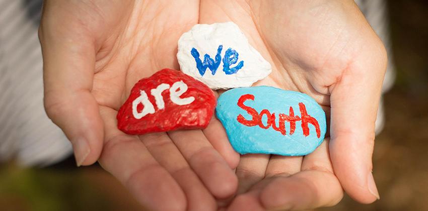 Hands holding We Are South painted rocks