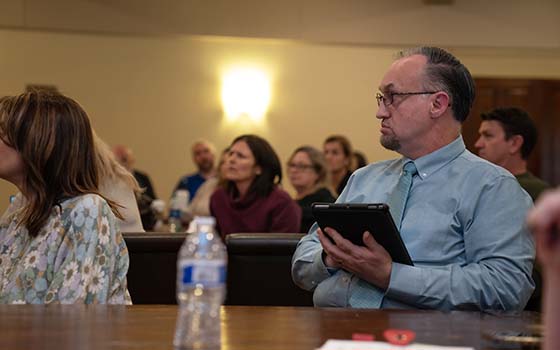 faculty members listening with attendee in foreground holding i-pad