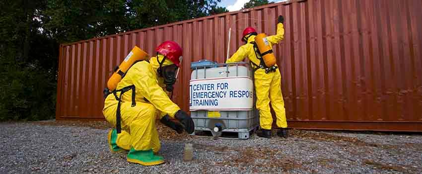 Two men in hazmat suits in front of storage container