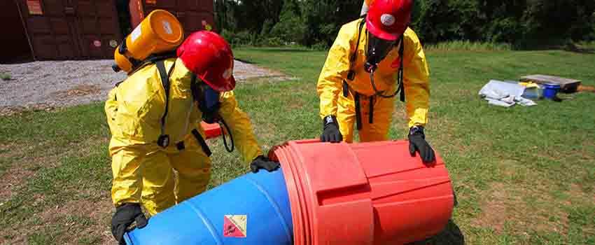 Two men in hazmat suits handling container