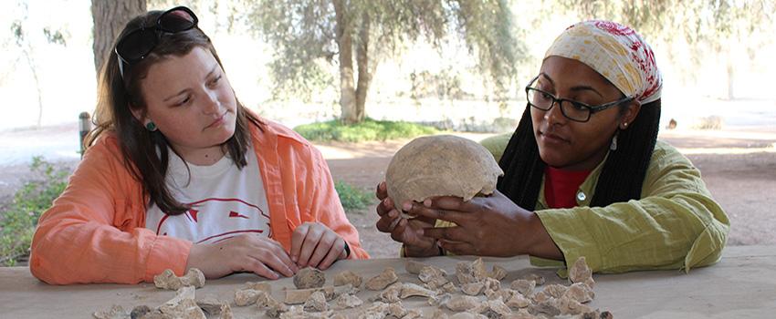 Two students studying a skull outside at a table