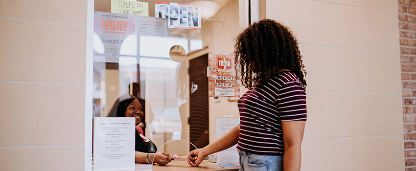 Female student reaching for ticket from woman working ticket counter