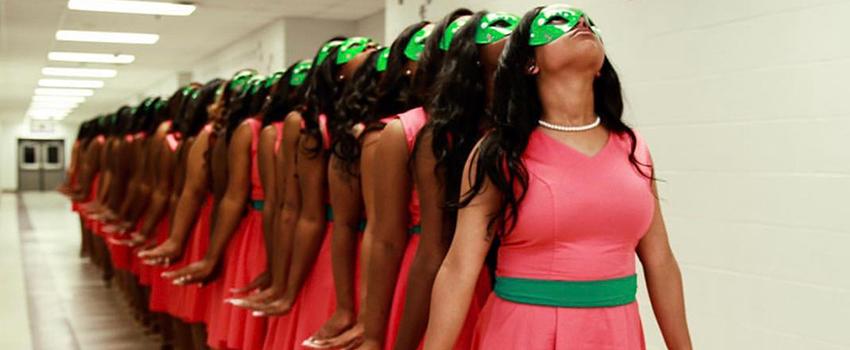 NPHC Studenst in pink dresses with green sashes looking up