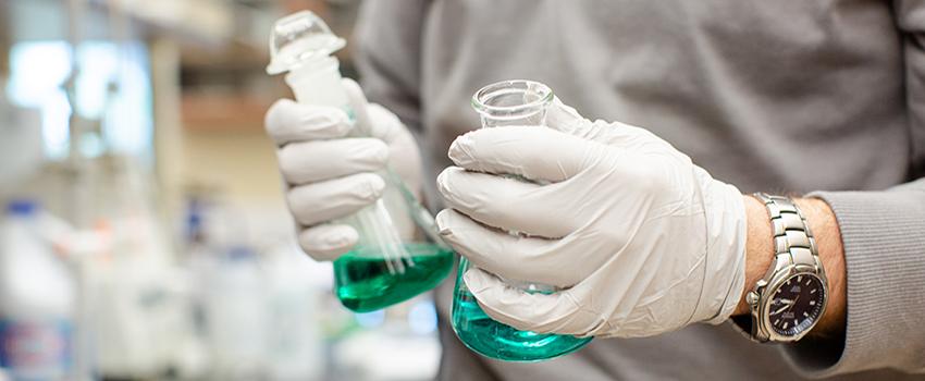 Hands with gloves holding two beakers.