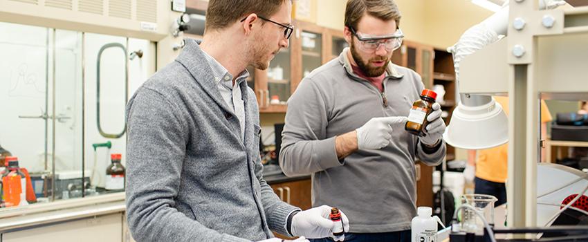 Two males looking at bottle in chemical engineering lab.