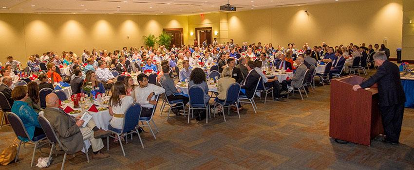 Crowd at engineering scholarship ceremony sitting at tables listening to speaker.