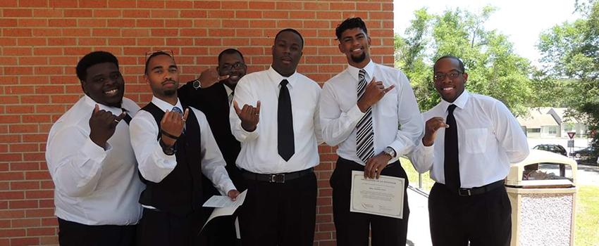 A group of male students holding up their pinky rings.