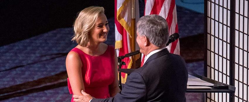 Female student walking across stage shaking dean's hand at graduation.