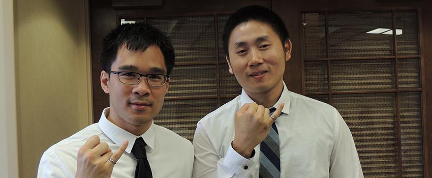 Two male students holding up their pinky rings.