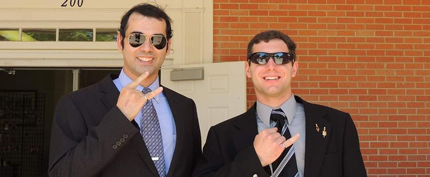 Two male students holding up their pinky rings.