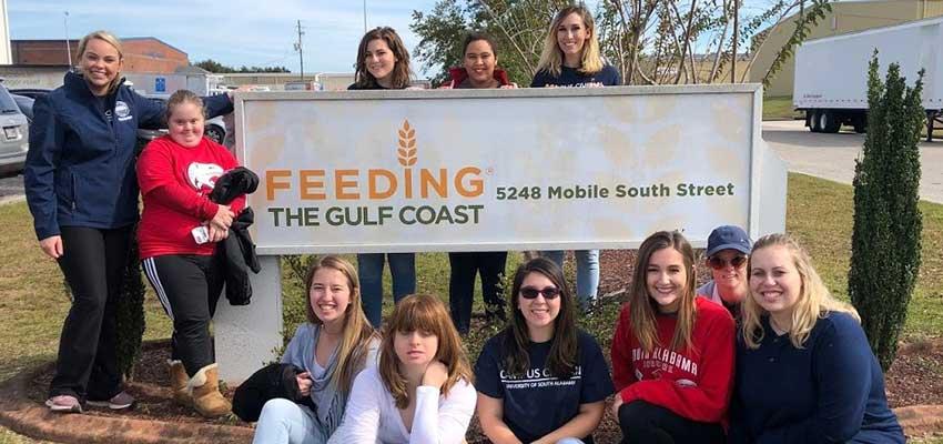 Mixed group of students at Feeding the Gulf Coast holding banner.