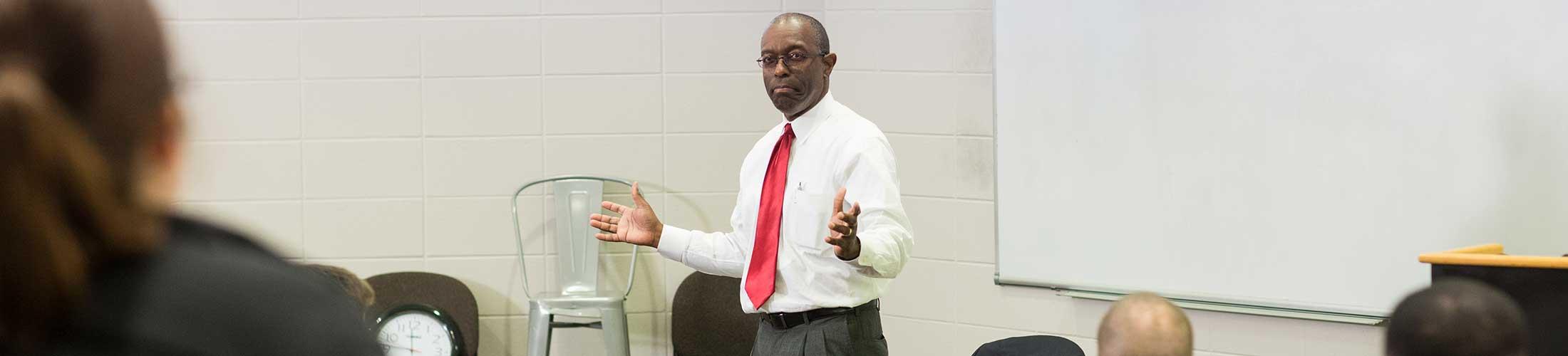 Dr. Williams in class speaking in front of board.