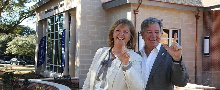 Mr. and Mrs. MacQueen in front of Alumni Center holding up J signs.