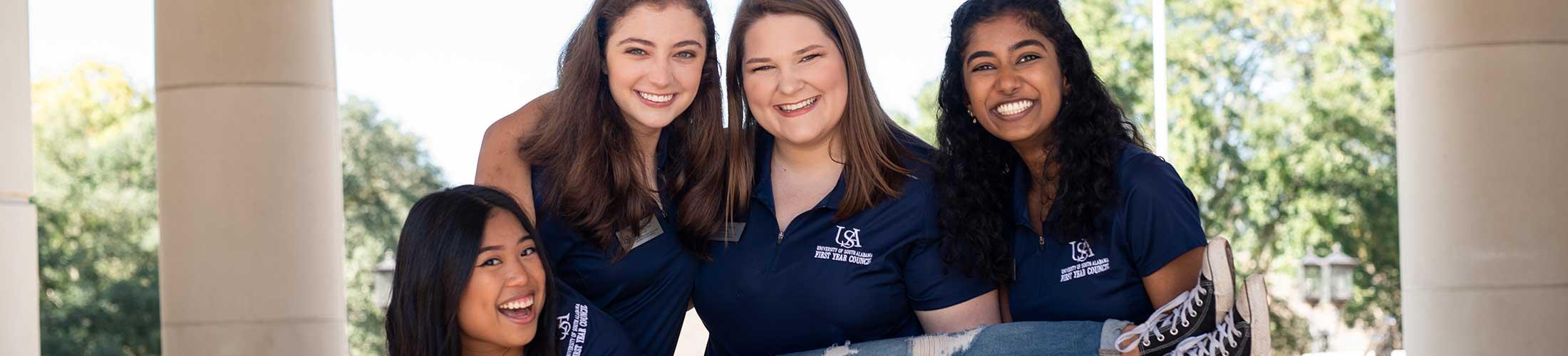 Three female FYC members holding one FYC member smiling.