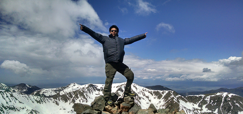 Male student standing on top of a mountain.