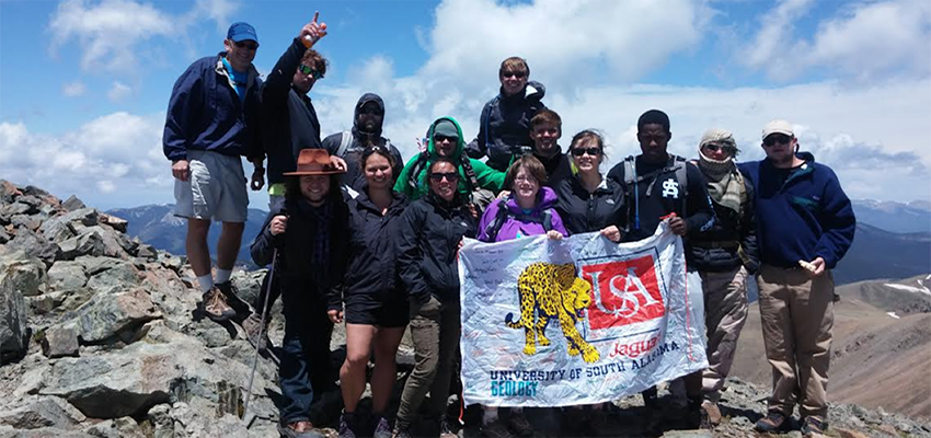 Group of students holding a USA flag out in the mountains.