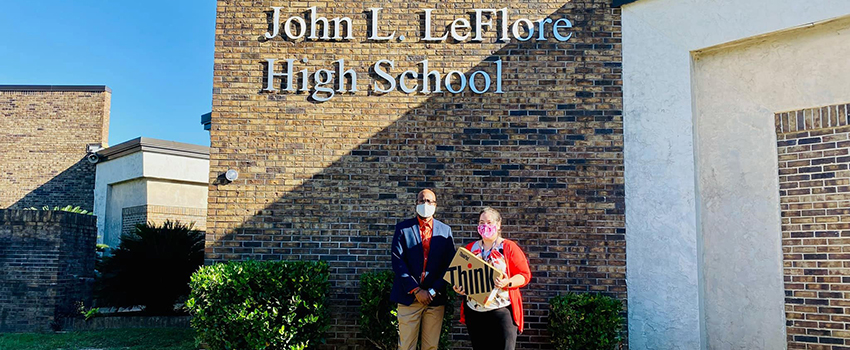 Two people standing in front of Leflore High School holding classroom materials.