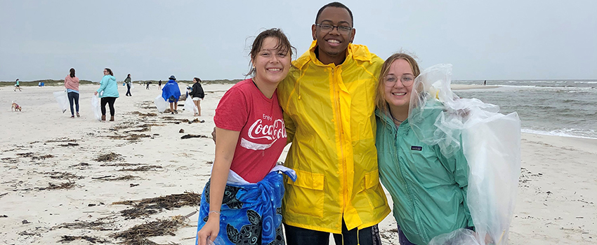 Three students picking up trash on the beach.