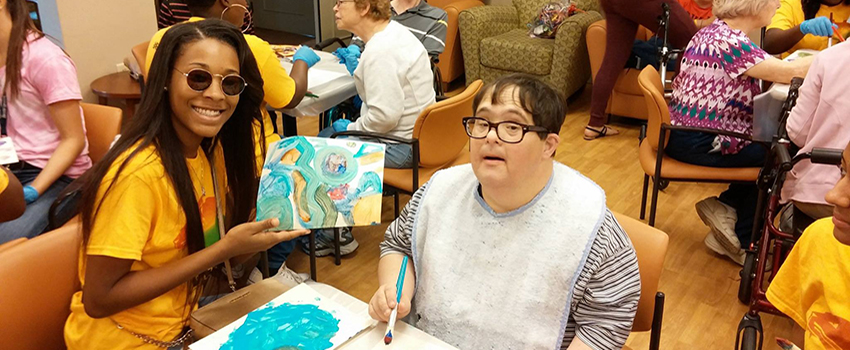 African American association student working on art project holding up a painting.