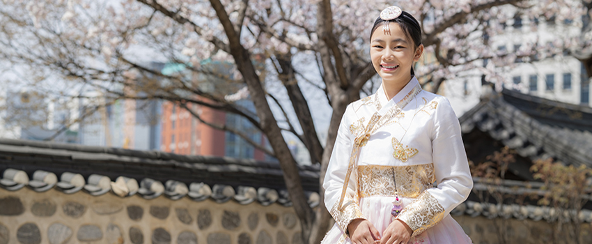 Woman in traditional Korean dress smiling outside.