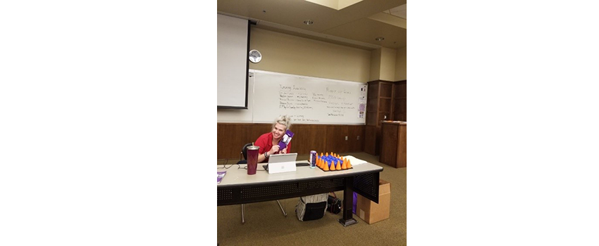 Person sitting at desk smiling with whiteboard behind her.