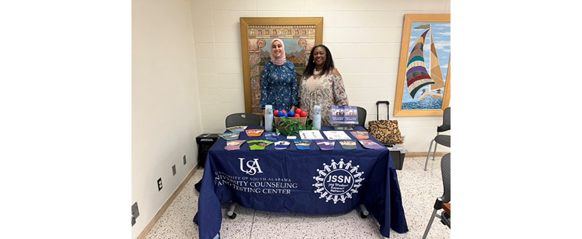 Two peer mentors standing behind table advertising for Peer Mentor counseling.