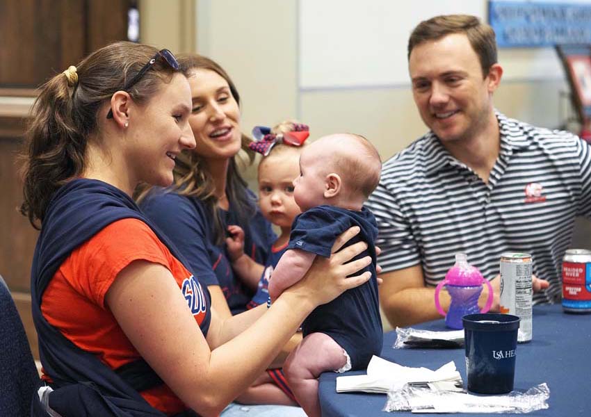 Woman holding a baby and people smiling looking on.