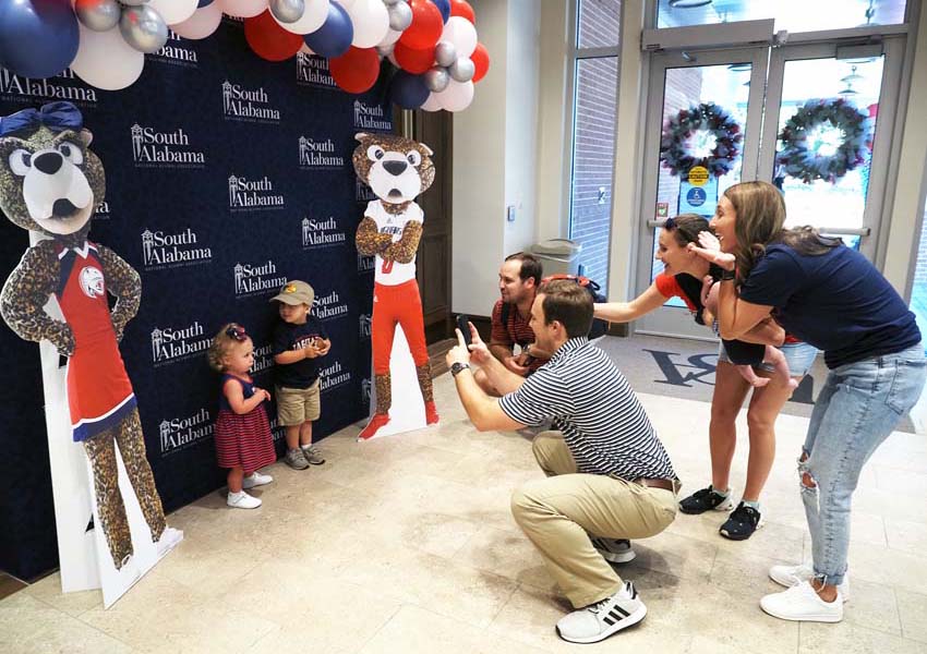 Parents taking pictures of their kids in front of South Alabama sign with cutouts of Southpaw and Ms. Pawla.
