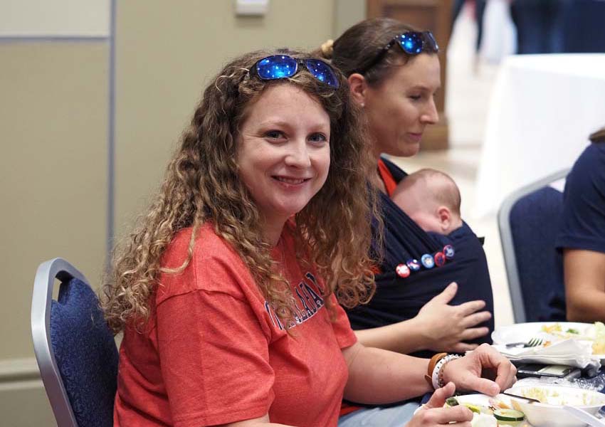 Woman smiling with lady with baby in background.