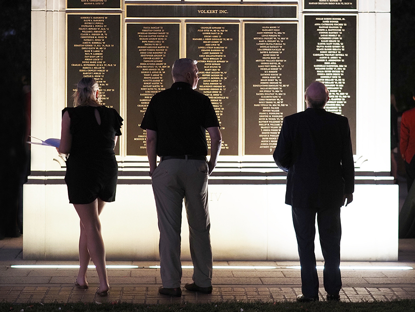 Three people in front of wall of honor.