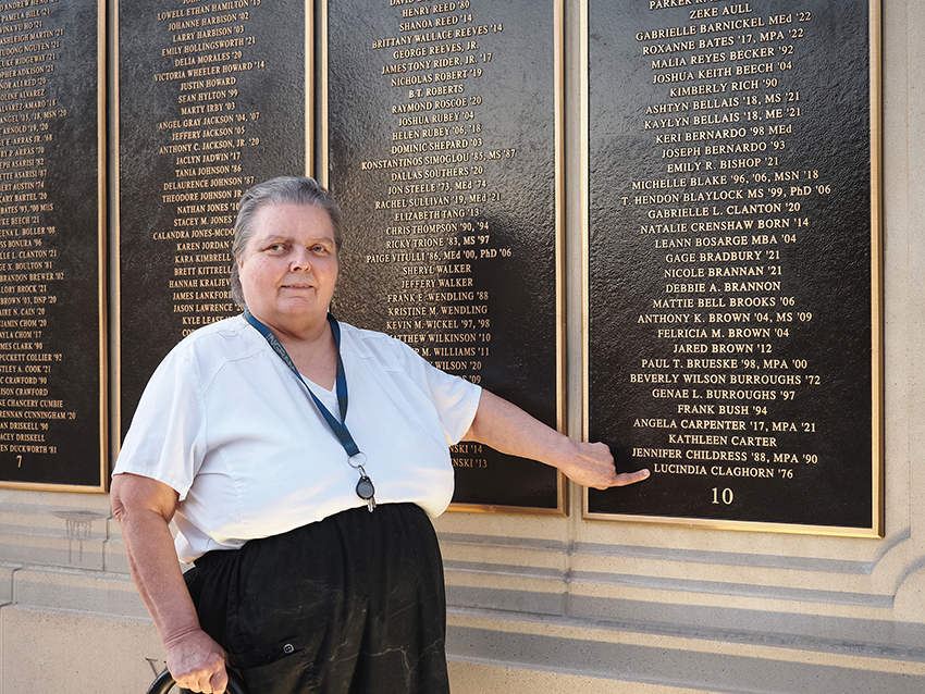 Woman pointing to name at wall of honor.