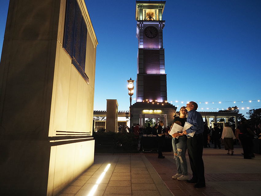 People looking at wall of honor at night with Moulton tower in background.