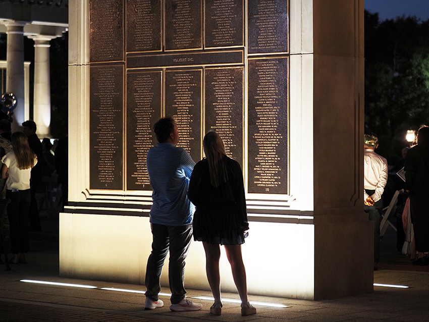 Two people in front of wall of honor.