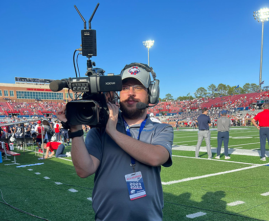 Passage USA Student with a video camera on gameday inside Hancock-Whitney Stadium.
