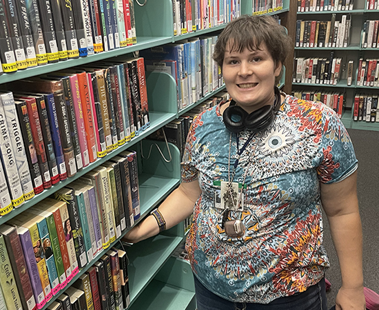 Errenia works at library in front of bookshelf.