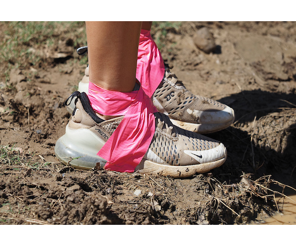 Tennis shoes with pink ribbon tied around legs.