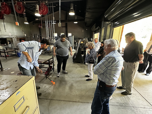 people being shown a demonstration of glass blowing in a glass working shop