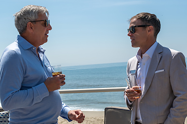 Two men talking with water in the background.