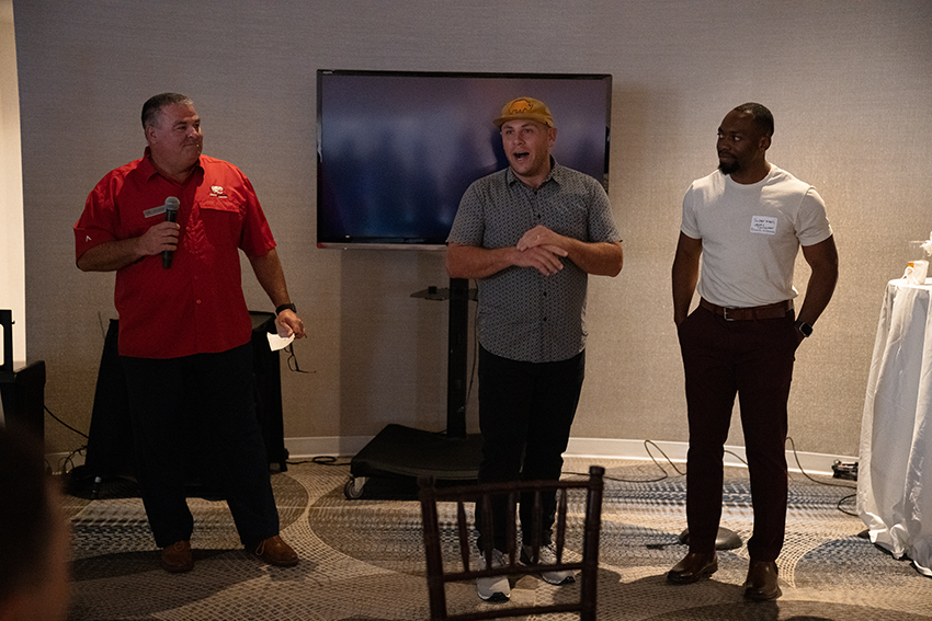 Man in red shirt speaking to two other alumni.