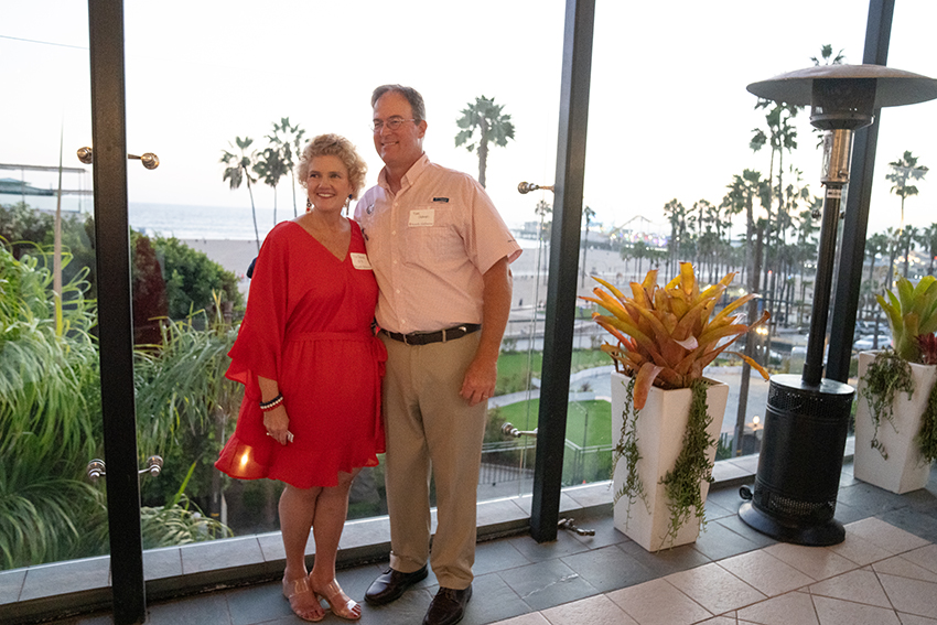 Couple in front of glass window with palm trees in the background. 