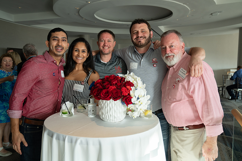 Five alumni behind table smiling.