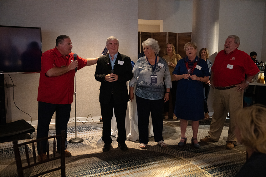 Man speaking holding microphone with others around him.