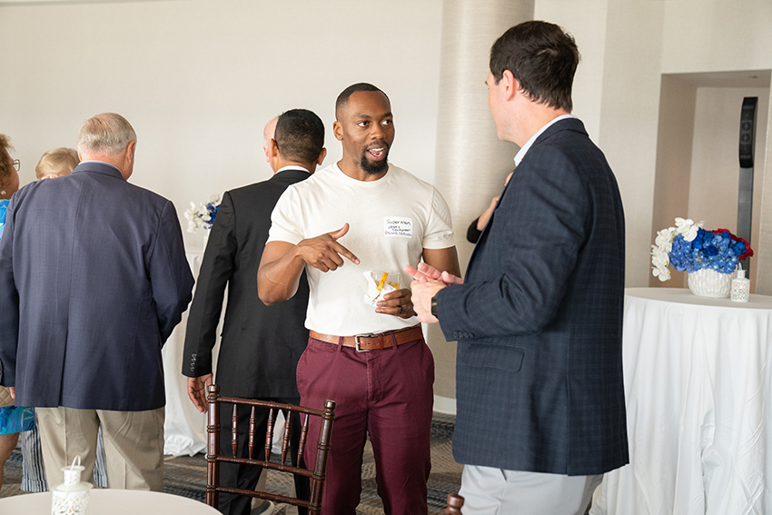 Man in maroon pants speaking to a fellow alumni.