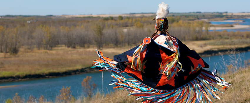 Native American in front of water in Native American attire.