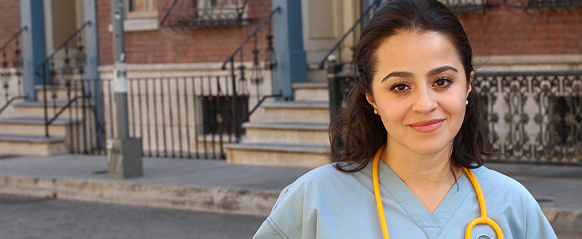 Native American in scrubs with stethoscope around neck standing outside in front of building.