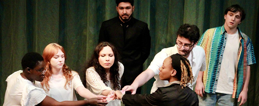 USA Students acting on stage in a play all reaching hands in a circle.