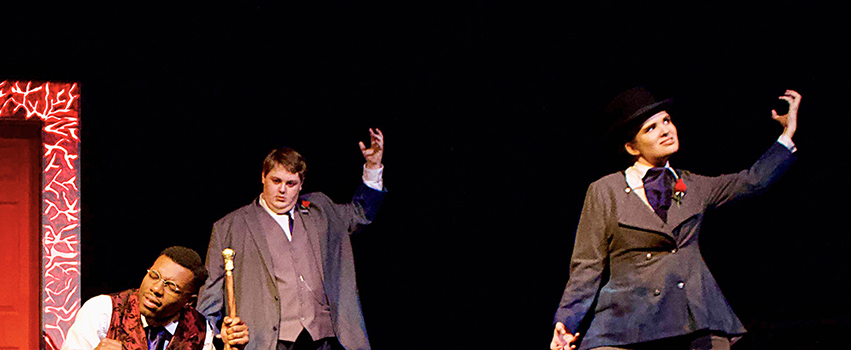 USA Students acting on stage in a play with players holding up hands while one is kneeling on the floor.