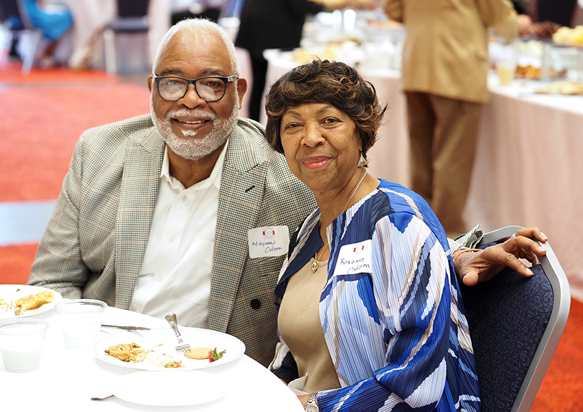 Two people sitting at table at event smiling.